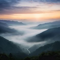 the sun is setting over some mountains with mist rolling in on them and fog covering the valley below