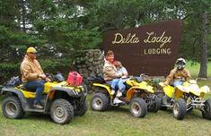 three people on four wheelers in front of a sign