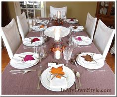 the table is set with white plates, silverware and autumn leaves on them for dinner