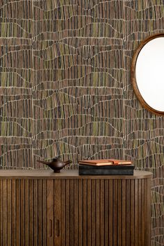 a wooden cabinet sitting next to a round mirror on top of a wallpapered wall