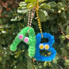 two stuffed animals hanging from a tree branch with beads on it's ear and eyes