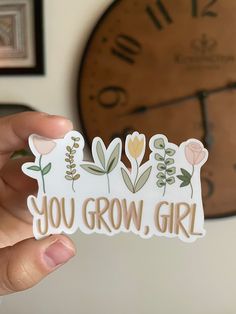 someone holding up a sticker that says you grow, girl with flowers on it