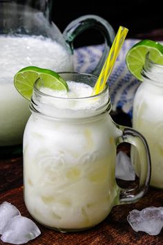 two mason jars filled with white liquid and lime slices on top of ice cubes