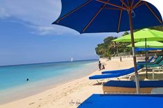 several lounge chairs and umbrellas on the beach with clear blue water in the background