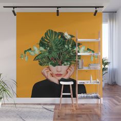 a wall mural with a woman's face and green leaves on it in front of a yellow background