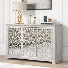 a white sideboard with an intricate design on the front and sides, next to a lamp