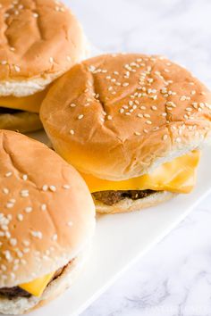 three cheeseburgers on a plate with sesame seeds