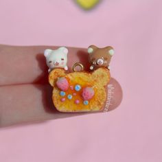 there is a tiny bear and cat brooch on someone's finger with pink background