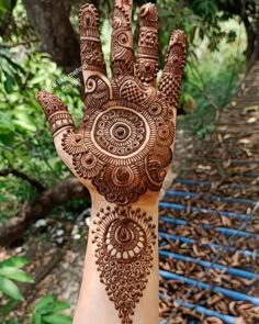 a hand with henna on it and some trees in the back ground behind it