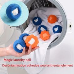 a hand holding a blue and orange ball in front of a dryer filled with white towels