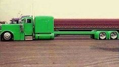 a green semi truck parked in front of a red building with a large trailer behind it