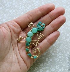 a hand holding a gold and green brooch with a lizard on it's back