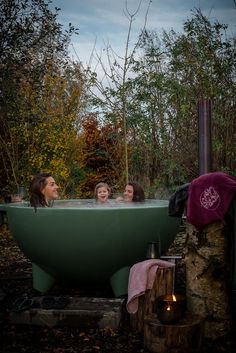 three women sitting in a green bathtub surrounded by trees