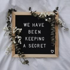 a sign that says we have been keeping a secret in front of some white flowers