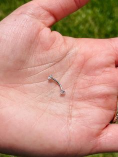 a person's left hand holding a tiny silver nose ring in their left hand