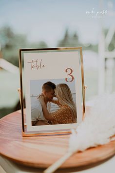 a couple kissing on the cheek in front of a wooden table with white feathers and a gold frame