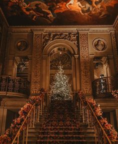 an ornate staircase leading up to a christmas tree in the middle of a room with paintings on the ceiling