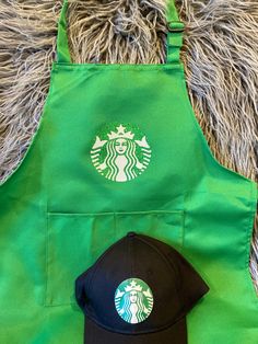 a green apron with a starbucks hat on it next to a black and white baseball cap