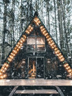 a small cabin in the woods is lit up with christmas lights and surrounded by snow