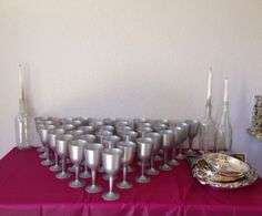 a table topped with lots of silver cups and saucers on top of a purple table cloth