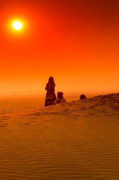 two people are sitting in the sand at sunset or sunrise, with one person looking up