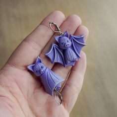 two little purple bats are being held in someone's hand and they look like they have been made out of polymer