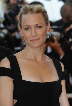 a woman in a black dress posing for the camera with cameras around her and onlookers behind her