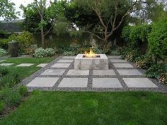 an outdoor fire pit in the middle of a garden with lots of grass and trees