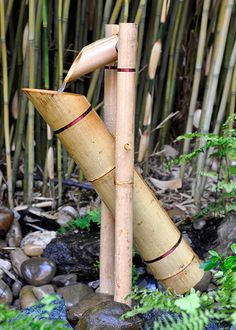 a bamboo sculpture is in the middle of some rocks and plants, with one wooden object sticking out of it's side