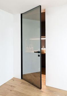 an open glass door in the corner of a room with wood floors and white walls