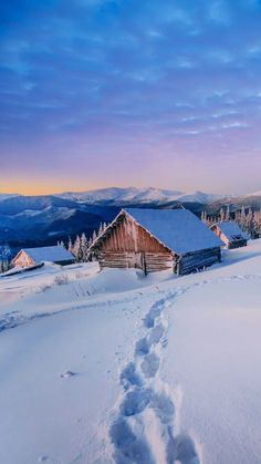 a cabin in the middle of a snow covered field with tracks leading to it and mountains in the distance