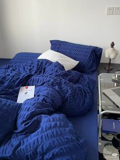 a blue comforter on a bed next to a table with a laptop and lamp