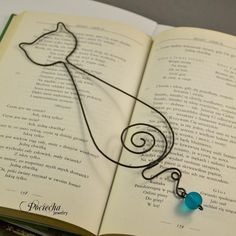 an open book with a wire drawing on the page and a blue bead hanging from it