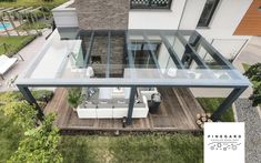 an aerial view of a modern house with glass walls and patio furniture in the backyard