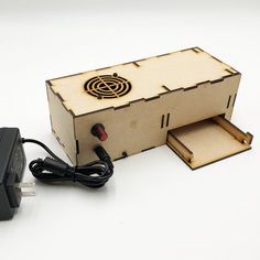 a wooden box with an electronic device in it sitting next to a charger and power cord