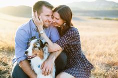 a man and woman sitting next to a dog in a field