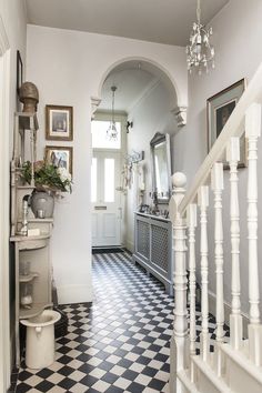 a hallway with black and white checkered flooring, chandelier and mirror