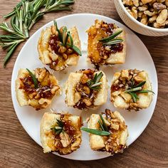 small appetizers are arranged on a white plate next to a bowl of nuts