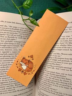 a bookmark with an image of a fox and leaves on it sitting next to a green plant