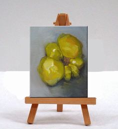 a small easel with a painting of yellow fruit on it's side, sitting in front of a white background