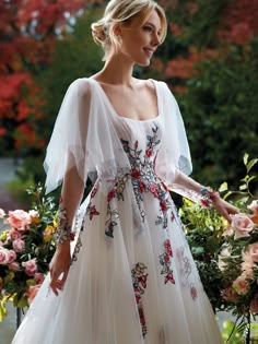 a woman in a white dress standing next to flowers