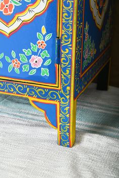 an ornate painted blue cabinet with flowers and leaves on the top, sitting on a striped tablecloth