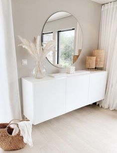 a white dresser sitting next to a window with a round mirror on top of it