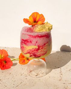 a drink with flowers on the side sitting on a table next to some rocks and sand