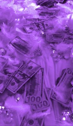 many dollars are scattered on top of each other with purple light in the background and white feathers