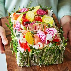 a wooden cutting board topped with a cake covered in candy and vegtables