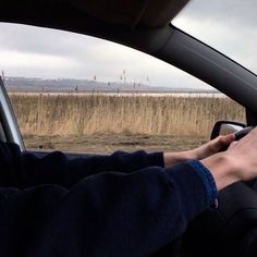 a person driving a car in front of a field with tall brown grass and trees