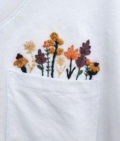 embroidered flowers are in the pocket of a white t - shirt that is being worn by someone