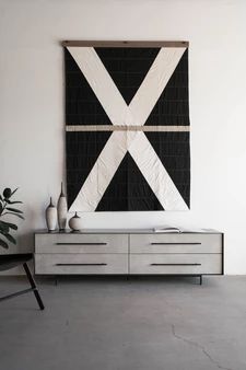 a large black and white quilt hanging on the wall next to a dresser with two vases