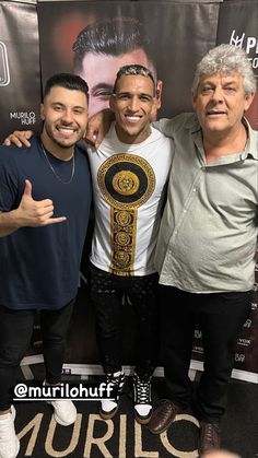 three men standing next to each other in front of a poster